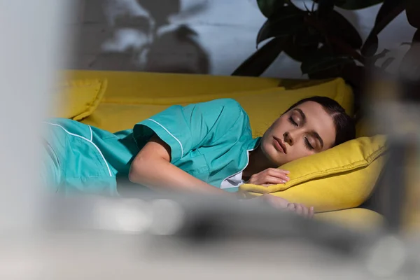 Вибірковий фокус привабливої медсестри в уніформі спить на жовтому дивані під час нічної зміни — стокове фото