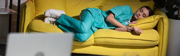 Panoramic shot of attractive nurse in uniform sleeping on yellow sofa during night shift — Stock Photo