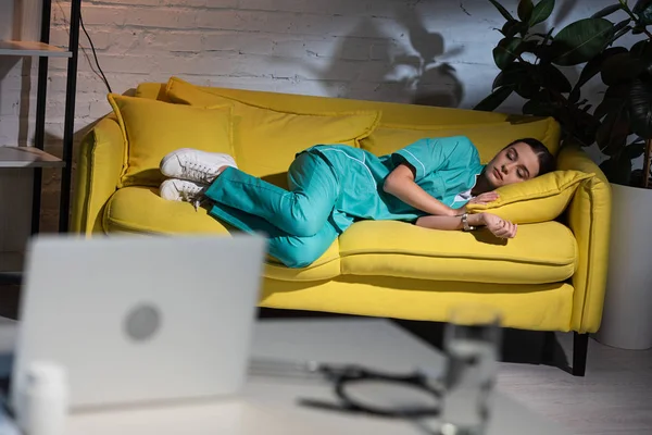 Selektiver Fokus der attraktiven Krankenschwester in Uniform, die während der Nachtschicht auf dem gelben Sofa schläft — Stockfoto