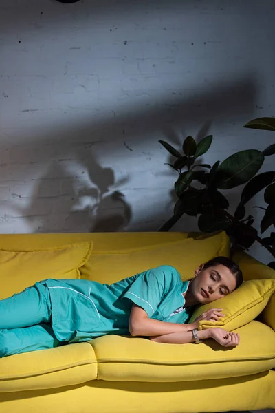 Infirmière attrayante en uniforme dormant sur un canapé jaune pendant le quart de nuit — Photo de stock
