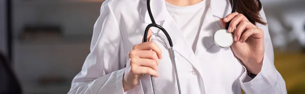 Vista recortada del médico de bata blanca sosteniendo estetoscopio durante el turno de noche - foto de stock