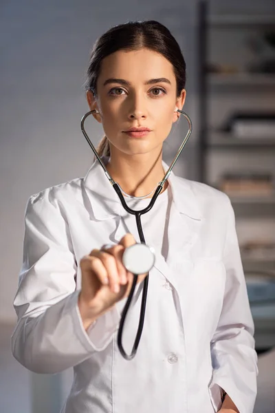 Selective focus of doctor in white coat holding stethoscope during night shift — Stock Photo