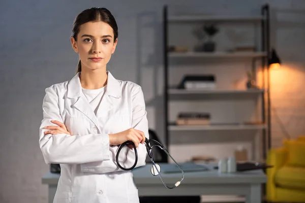 Attractive doctor in white coat holding stethoscope during night shift — Stock Photo