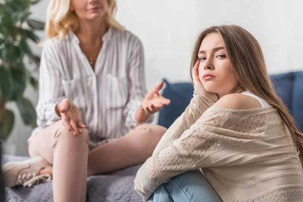 Enfoque selectivo de la chica ofendida mirando a la cámara cerca de la madre mostrando gesto encogiéndose de hombros - foto de stock