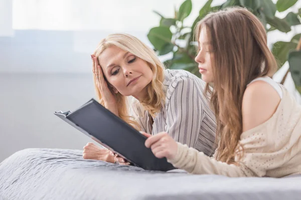 Reife Frau mit kleiner Tochter liegt auf Bett und schaut sich Fotoalbum an — Stockfoto