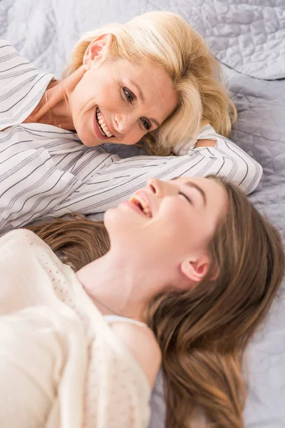 Selektiver Fokus einer glücklichen reifen Frau, die auf ihre hinkende Tochter blickt, während sie zusammen im Bett liegt — Stockfoto