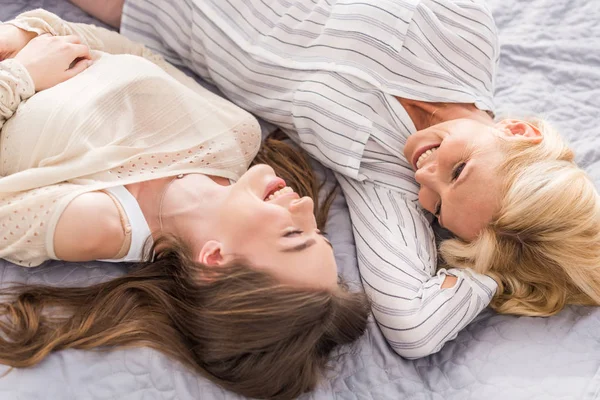 Overhead view of happy mother looking at laghing daughter while lying on bed together — Stock Photo