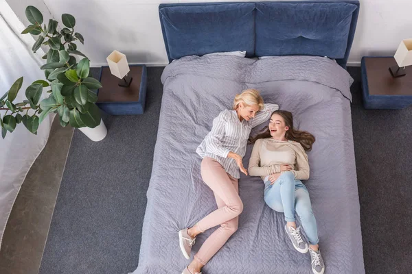 Vue de dessus de la mère et de la fille heureuses parlant et riant tout en étant couché sur le lit — Photo de stock