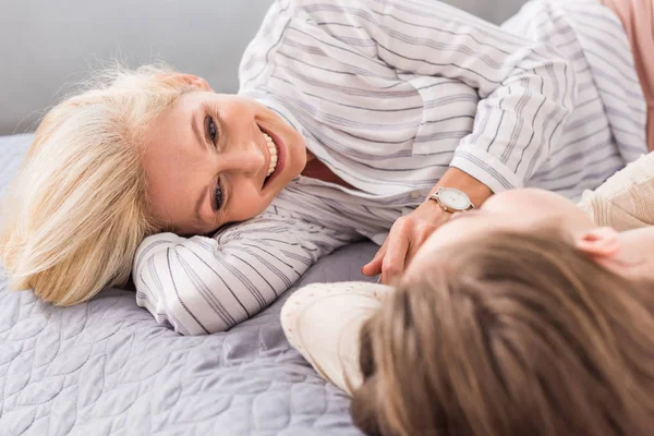 Селективное внимание счастливой женщины, улыбающейся и смотрящей на дочь, лежащую на кровати — стоковое фото