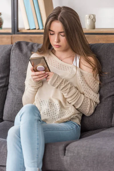 Pretty girl using smartphone while sitting on sofa at home — Stock Photo