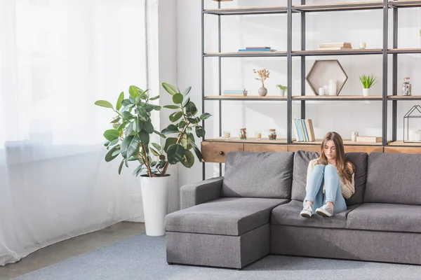 Pretty girl using smartphone while sitting on sofa in living room — Stock Photo