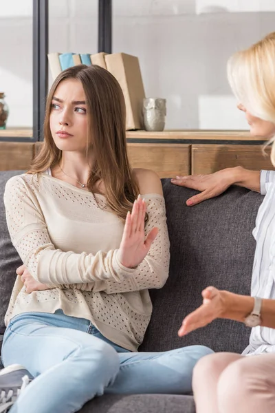 Beleidigtes Mädchen zeigt Stopp-Geste und schaut weg, während es neben sprechender Mutter sitzt — Stockfoto