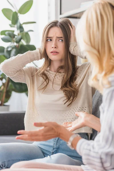 Upset girl plugging ears with hands while looking at talking mother — Stock Photo