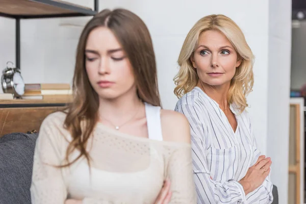 Selective focus of serious mature woman sitting with crossed arms and looking at offended daughter — Stock Photo