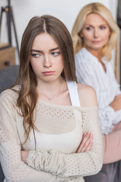 Fuoco selettivo della ragazza offesa seduta con le braccia incrociate vicino alla madre seria — Foto stock