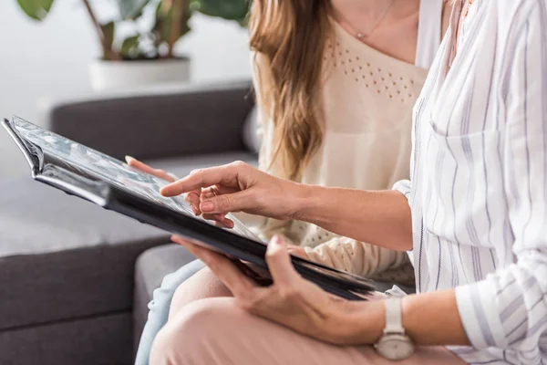 Abgeschnittene Ansicht einer Frau, die mit dem Finger auf ein Fotoalbum zeigt, während sie in der Nähe ihrer Tochter sitzt — Stockfoto