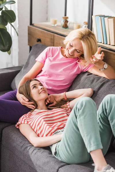 Mãe feliz e filha falando enquanto descansam no sofá juntos — Fotografia de Stock