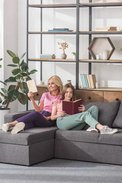 Glückliche Mutter und Tochter sitzen auf dem Sofa im Wohnzimmer und lesen Bücher — Stockfoto