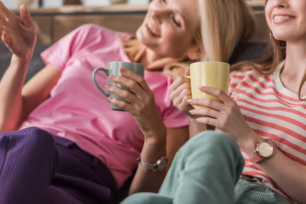 Foyer sélectif de femme joyeuse pointant avec la main tout en étant assis près de la fille avec des tasses à thé — Photo de stock