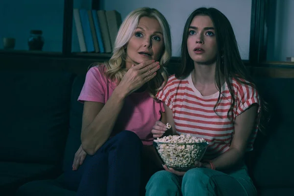 Madre e hija enfocadas viendo la televisión y comiendo palomitas de maíz - foto de stock