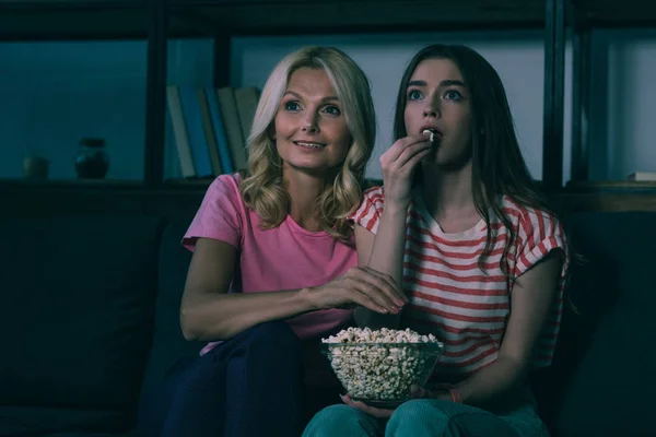 Внимательные мать и дочь смотрят телевизор и едят попкорн — стоковое фото