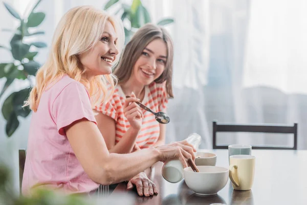 Foyer sélectif de la mère et de la fille gaies assis à la table de cuisine et prendre le petit déjeuner — Photo de stock