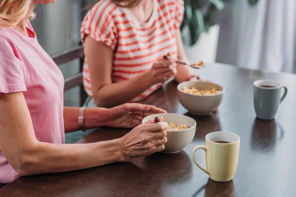 Vista ritagliata di madre e figlia seduti al tavolo della cucina e fare colazione — Foto stock