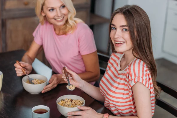 Foco seletivo da menina sorrindo para a câmera enquanto toma café da manhã com a mãe — Fotografia de Stock