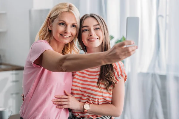 Pretty, young girl hugging happy mother taking selfie on smartphone — Stock Photo