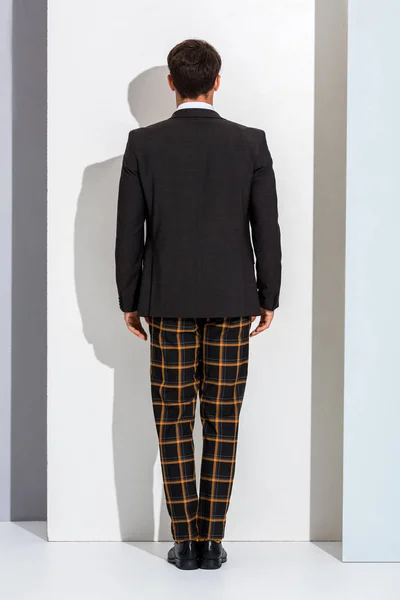 Visão traseira do homem elegante em calças xadrez em pé sobre branco e cinza — Fotografia de Stock