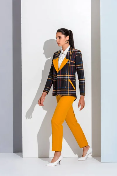 Stylish girl in checkered formal wear walking on white and grey — Stock Photo