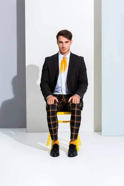 Красивый и стильный мужчина, сидящий на желтом стуле на белом и сером — стоковое фото