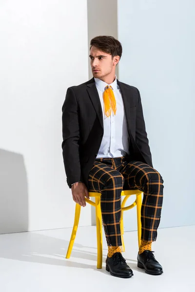 Stilvoller Mann sitzt auf gelbem Stuhl auf weiß und grau — Stockfoto