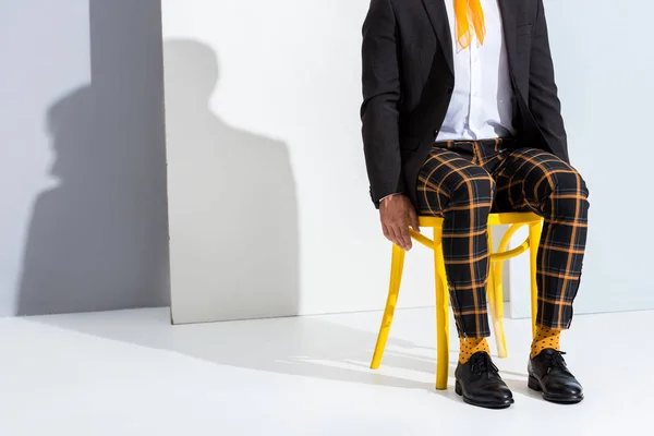 Cropped view of stylish man sitting on yellow chair on white and grey — Stock Photo