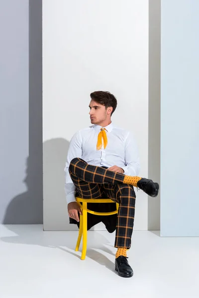 Handsome man posing while sitting on yellow chair on white and grey — Stock Photo