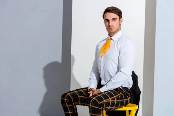Мужчина позирует, сидя на желтом стуле на белом и сером — стоковое фото
