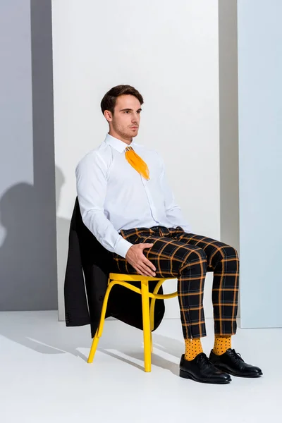 Молодий чоловік позує, сидячи на жовтому стільці на білому і сірому — стокове фото