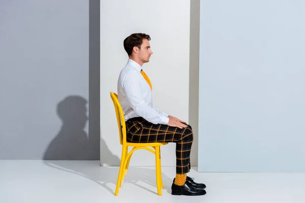 Vista lateral del hombre en pantalones a cuadros sentados en blanco y gris - foto de stock