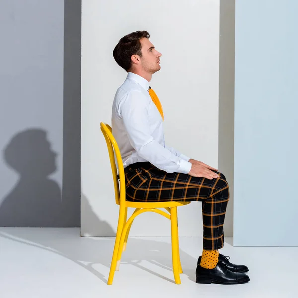 Vista lateral de homem bonito em calças xadrez sentado em branco e cinza — Fotografia de Stock