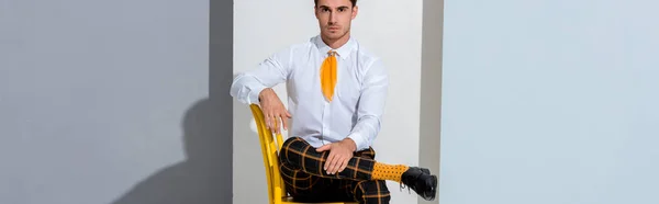 Панорамный снимок положительного человека в клетчатых брюках, сидящих на белом и сером — стоковое фото