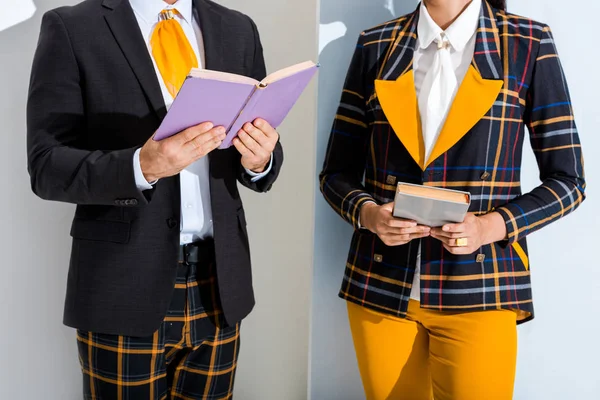 Ausgeschnittene Ansicht eines Mannes, der ein Buch in der Nähe eines stilvollen Mädchens auf Weiß und Grau hält — Stockfoto