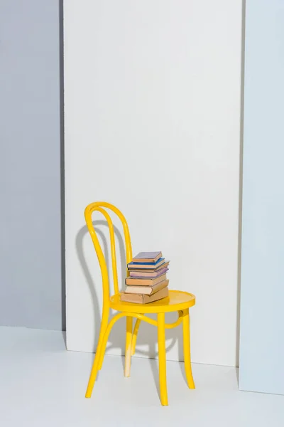 Sedia gialla con libri su bianco e grigio — Foto stock