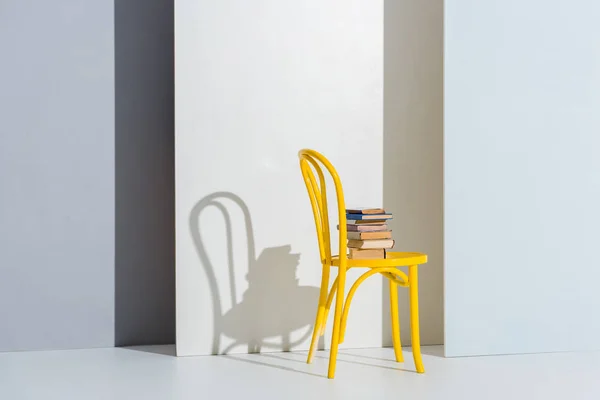 Books on yellow chair on white and grey with copy space — Stock Photo