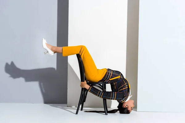 Jolie femme couchée sur chaise et posant sur gris et blanc — Photo de stock