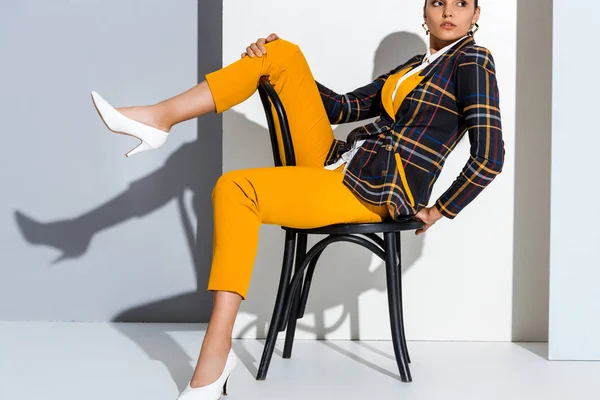 Cropped view of young woman sitting on chair and posing on grey and white — Stock Photo