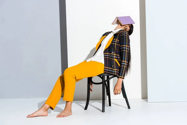 Woman sitting on chair with purple book on grey and white — Stock Photo