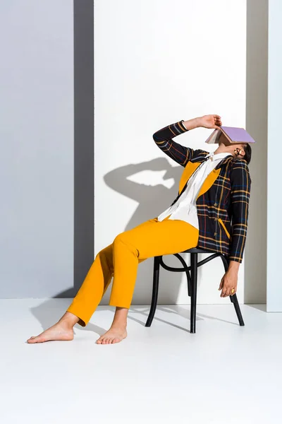 Jeune femme assise sur chaise avec livre violet sur gris et blanc — Photo de stock