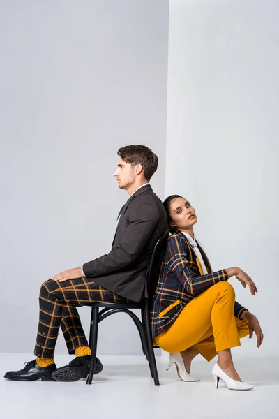 Stylische Frau posiert neben Mann auf Stuhl auf weiß — Stockfoto