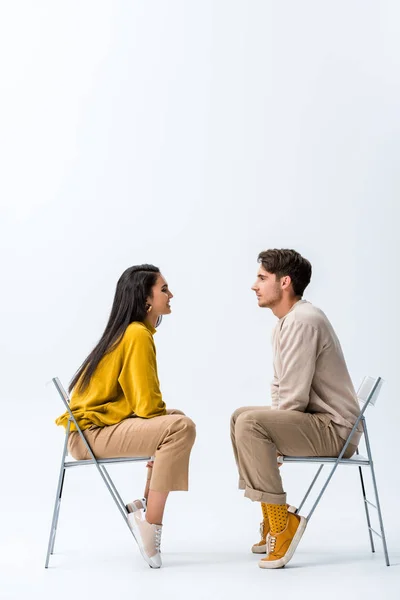 Vista lateral del hombre guapo sentado en la silla cerca de la mujer alegre en blanco - foto de stock