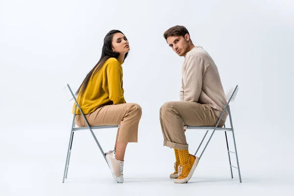 Young attractive woman sitting on chair near handsome man on white — Stock Photo